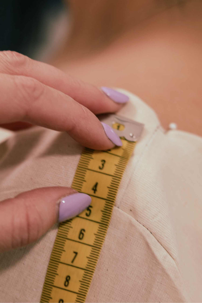 Leim Sewing workshops - jumpsuit sewing workshops - Hand with measuring tape on a garment, teaching the students how to  tailor the jumpsuit to their body