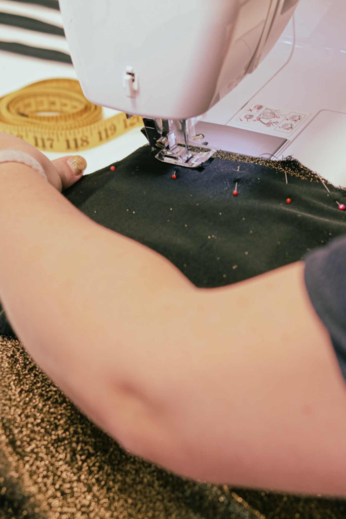 Leim Sewing workshops - jumpsuit sewing workshops - Person sewing on a piece of fabric with a sewing machine, using a measuring tape in the background.